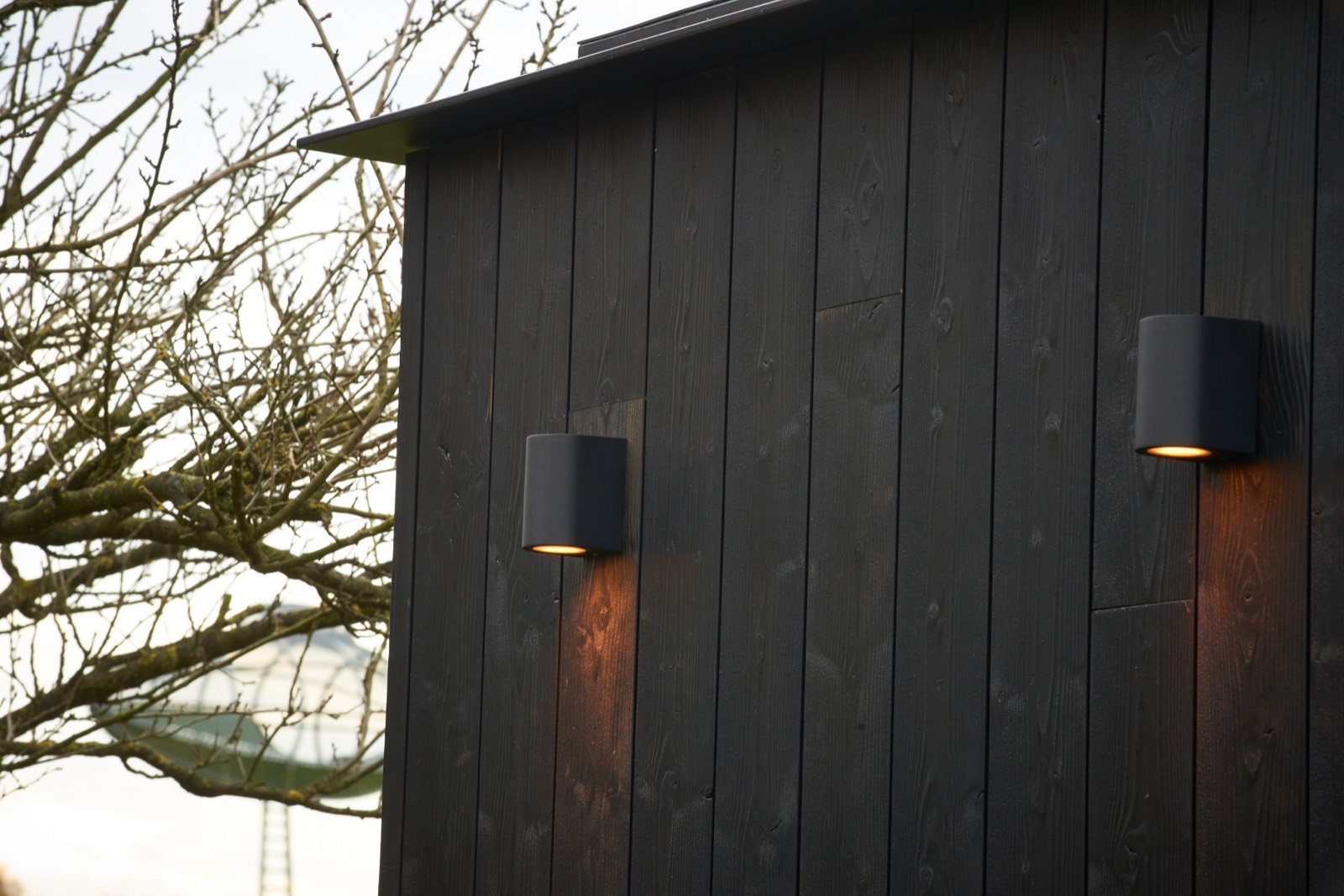 Zwarte thermowood-gevel van een Skelp-buitensauna met warme wandverlichting in de avond