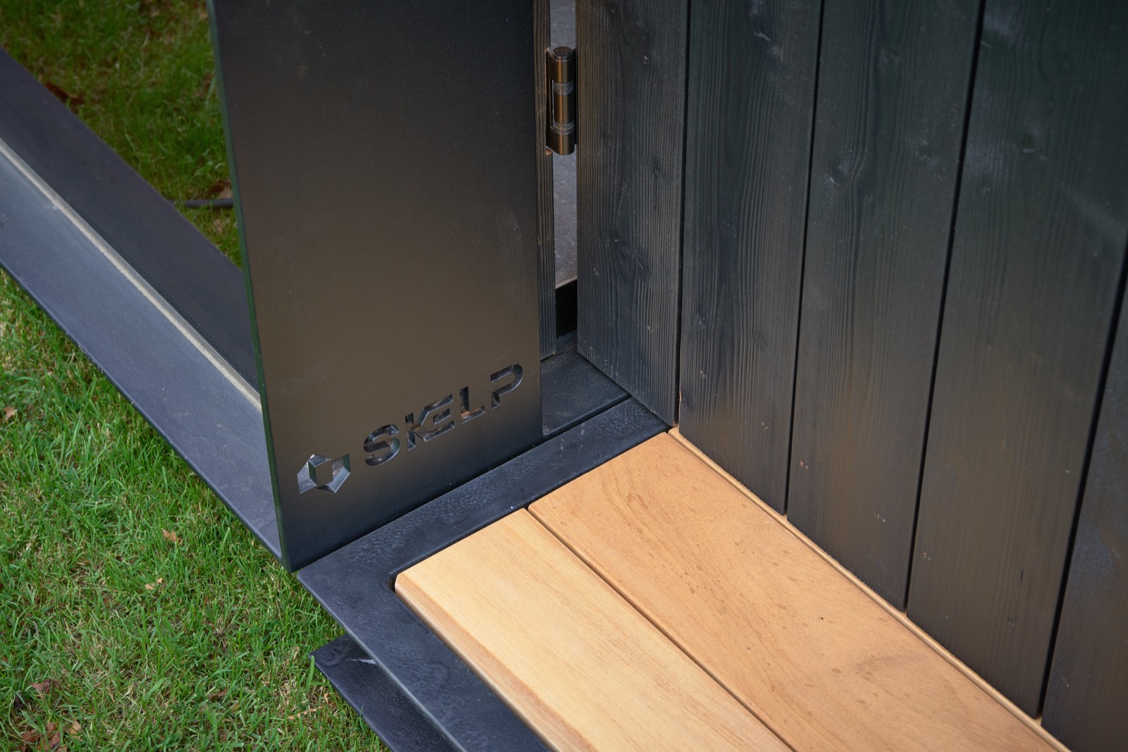 Detail van het lasergesneden Skelp-logo en het thermowood terras van een buitensauna op maat