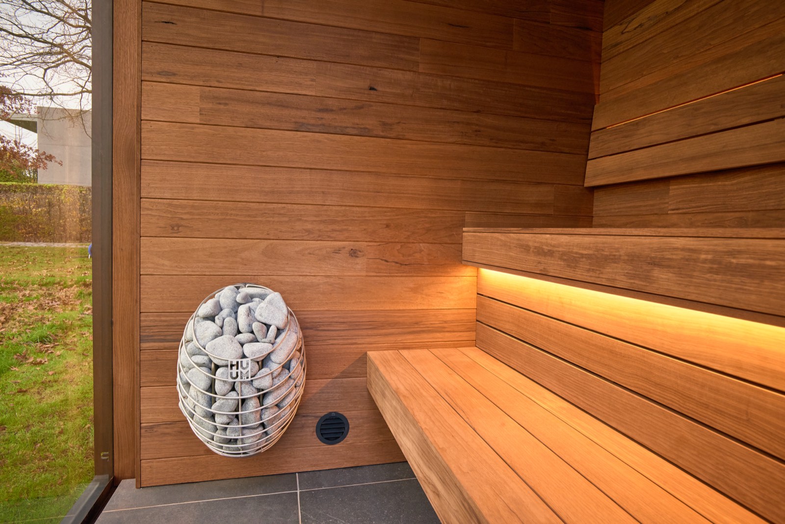 Warm verlicht interieur van een Skelp-buitensauna met thermowood-bank en zicht op de tuin